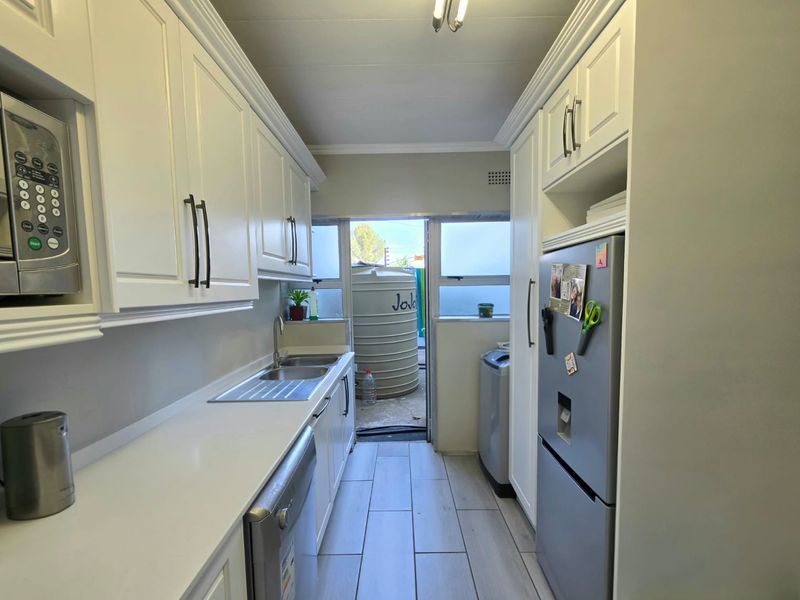 A clean, modern galley-style kitchen featuring white cabinetry, integrated microwave, stainless steel sink, and tiled flooring with direct access to the rear exterior.