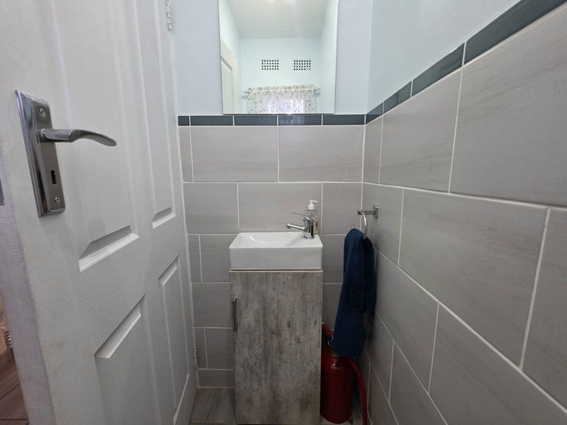A compact guest bathroom featuring modern grey wall tiling, a vanity cabinet with a basin, and a wall-mounted mirror.