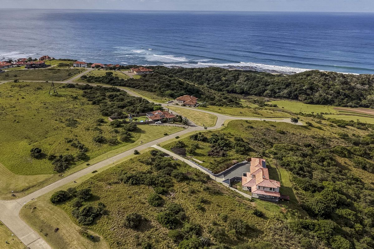 An aerial view of a coastal residential estate featuring paved roads, undeveloped land, and established homes overlooking the ocean.