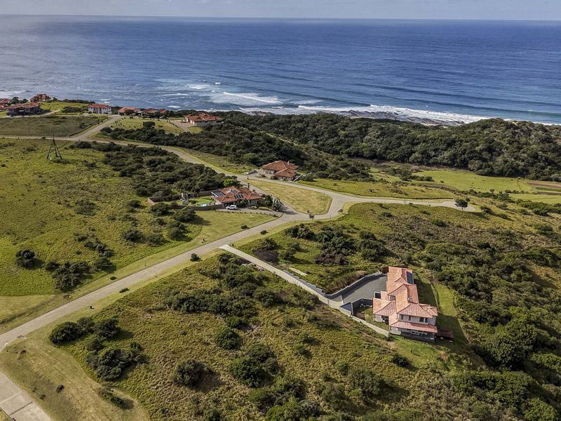 An aerial view of a coastal residential estate featuring paved roads, undeveloped land, and established homes overlooking the ocean.