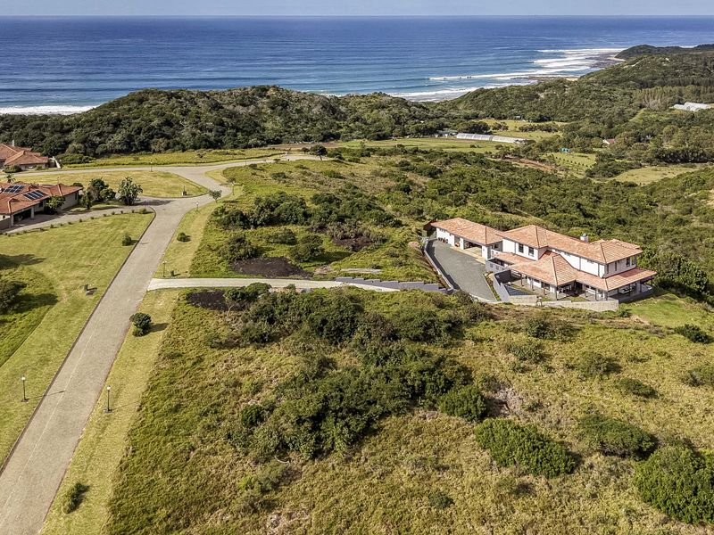 Aerial view of a residential property situated in a coastal estate, featuring expansive natural surroundings and proximity to the ocean.