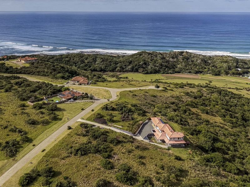 Aerial view of a residential property situated in a coastal estate, featuring paved access roads and surrounding natural landscape.