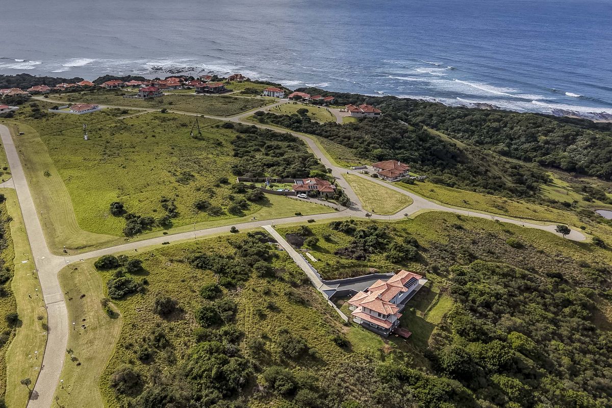 An aerial view of a coastal residential estate featuring paved roads, landscaped grounds, and established homes overlooking the ocean.