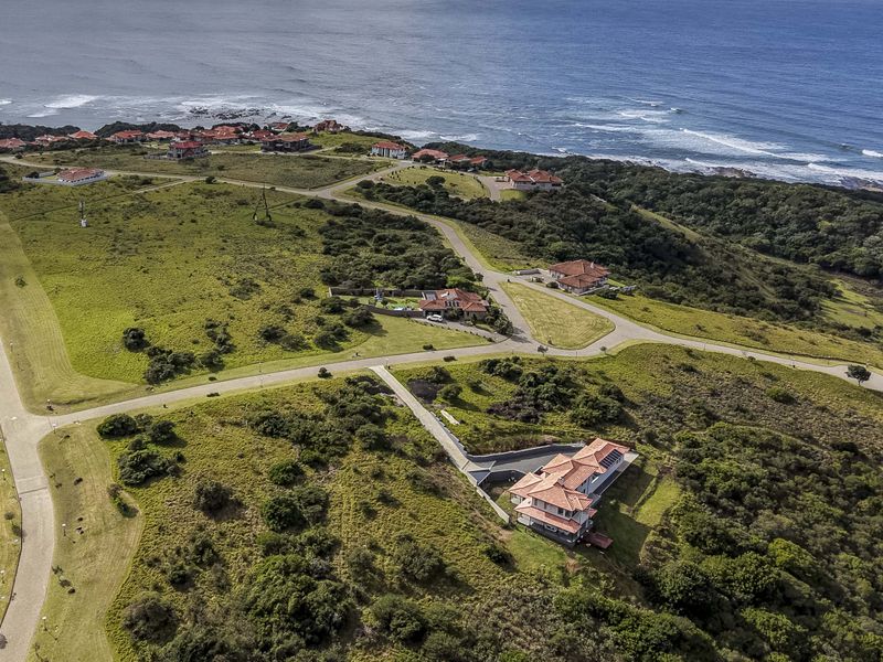 An aerial view of a coastal residential estate featuring paved roads, landscaped grounds, and established homes overlooking the ocean.