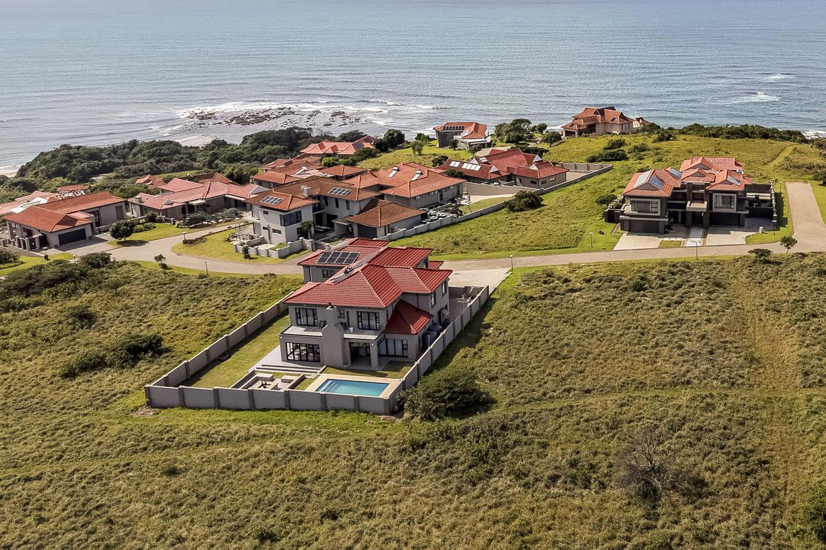 Aerial view of a coastal residential estate featuring modern homes with tiled roofs, private swimming pools, and landscaped grounds overlooking the ocean.
