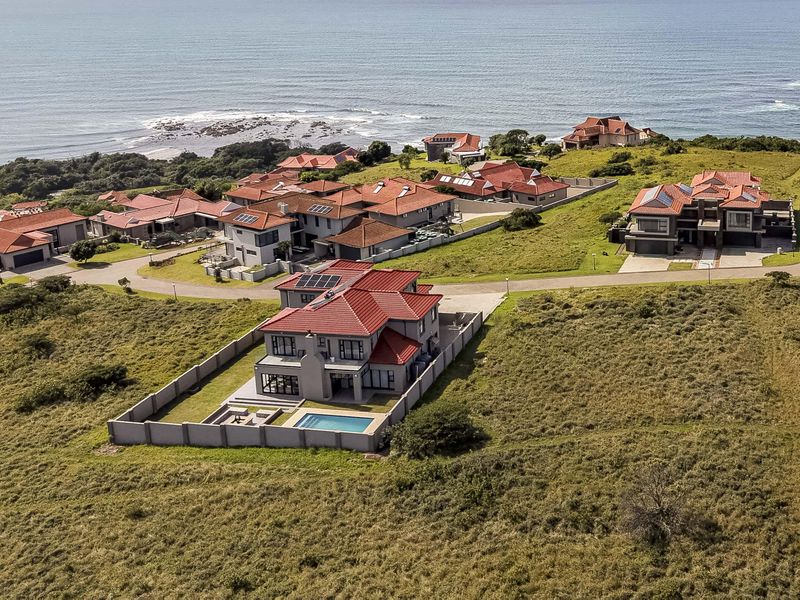 Aerial view of a coastal residential estate featuring modern homes with tiled roofs, private swimming pools, and landscaped grounds overlooking the ocean.