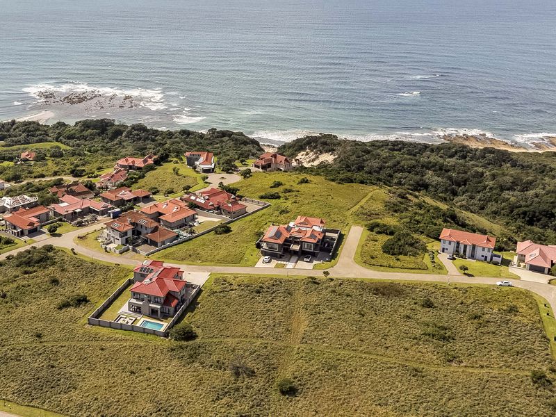 Aerial view of a coastal residential estate featuring multiple homes, paved roads, and undeveloped land plots overlooking the ocean.