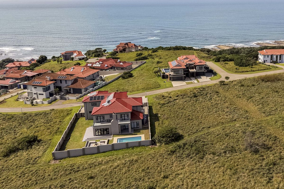 Aerial view of a coastal residential estate featuring multiple detached homes, paved access roads, and proximity to the ocean.