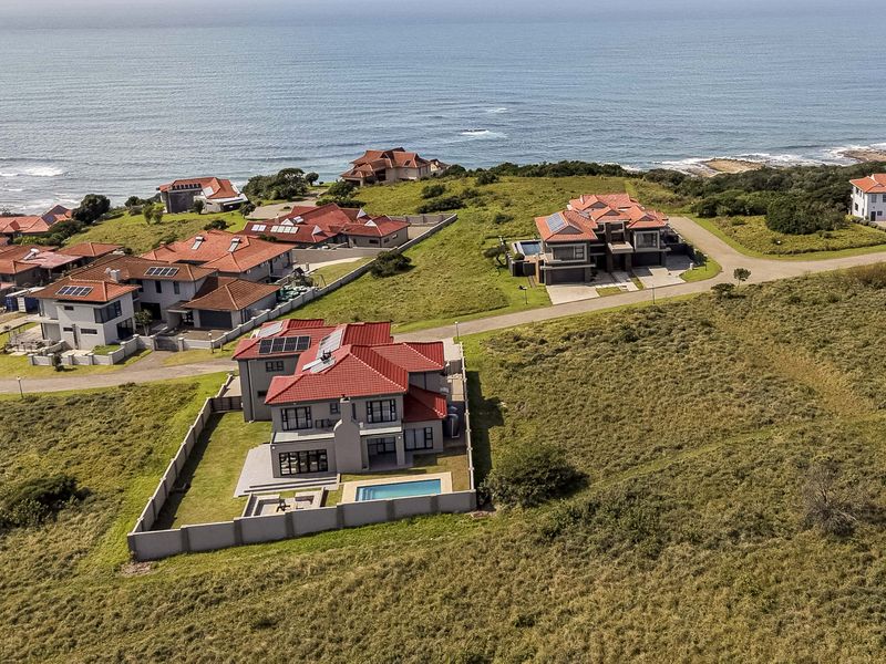 Aerial view of a coastal residential estate featuring multiple detached homes, paved access roads, and proximity to the ocean.