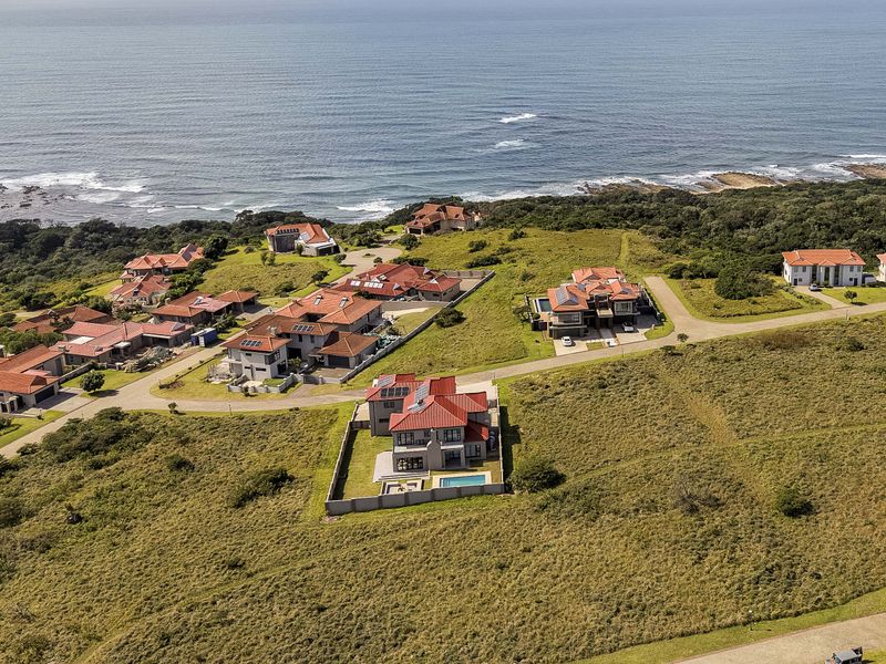 Aerial view of a coastal residential estate featuring multiple detached homes, paved access roads, and proximity to the ocean.