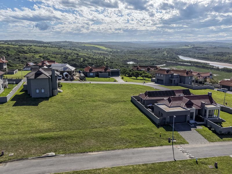 An aerial view of a vacant residential plot situated within a developed estate, featuring surrounding homes and access to a paved road.