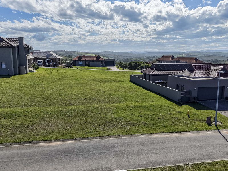 An elevated aerial view of a vacant residential plot featuring a well-maintained grass lawn, boundary walls, and surrounding neighborhood infrastructure.