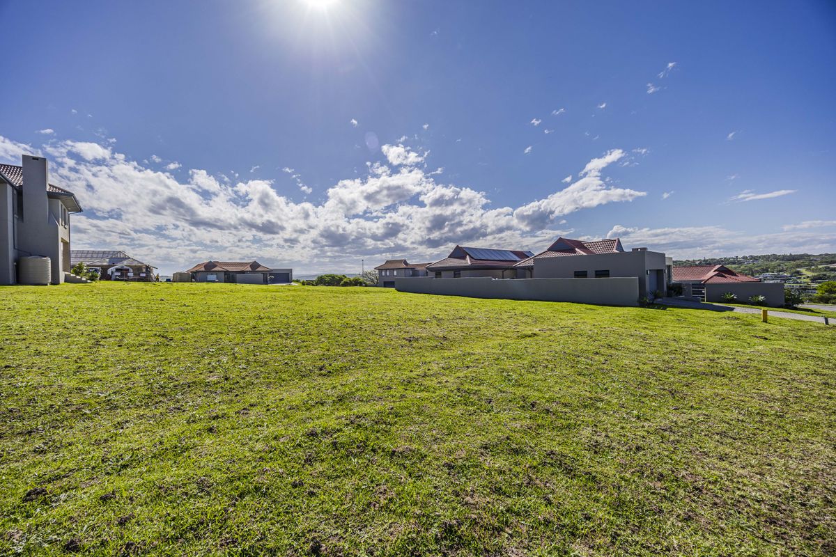A spacious vacant residential plot featuring a well-maintained grass lawn and boundary wall, situated within a developed neighborhood setting.