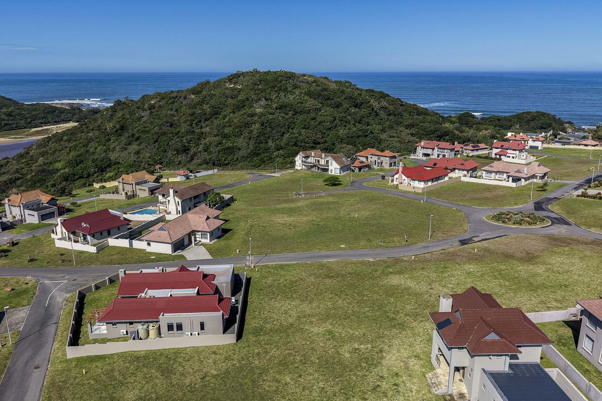 An aerial view of a residential estate featuring vacant plots, paved roads, and surrounding coastal landscape.