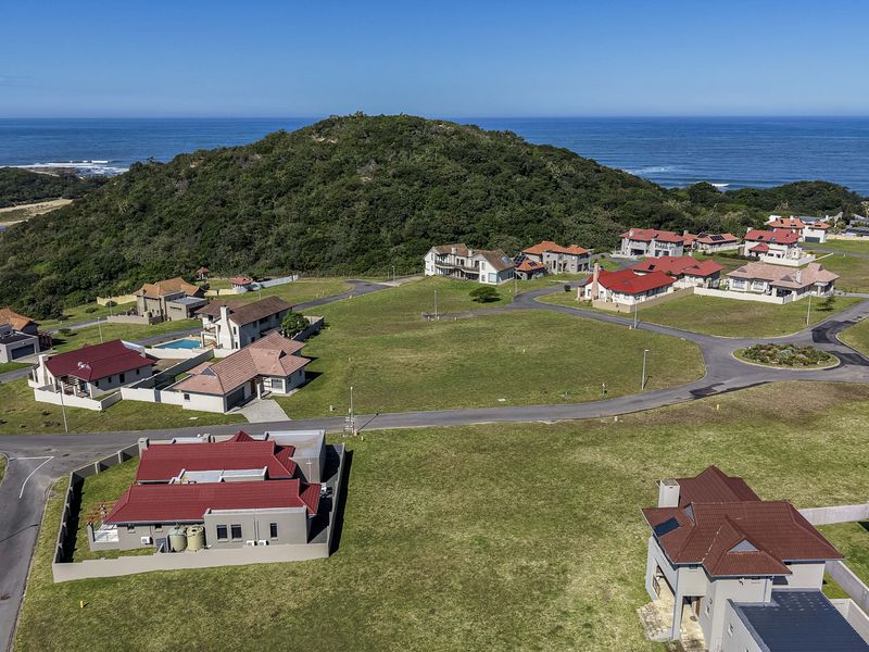 An aerial view of a residential estate featuring vacant plots, paved roads, and surrounding coastal landscape.