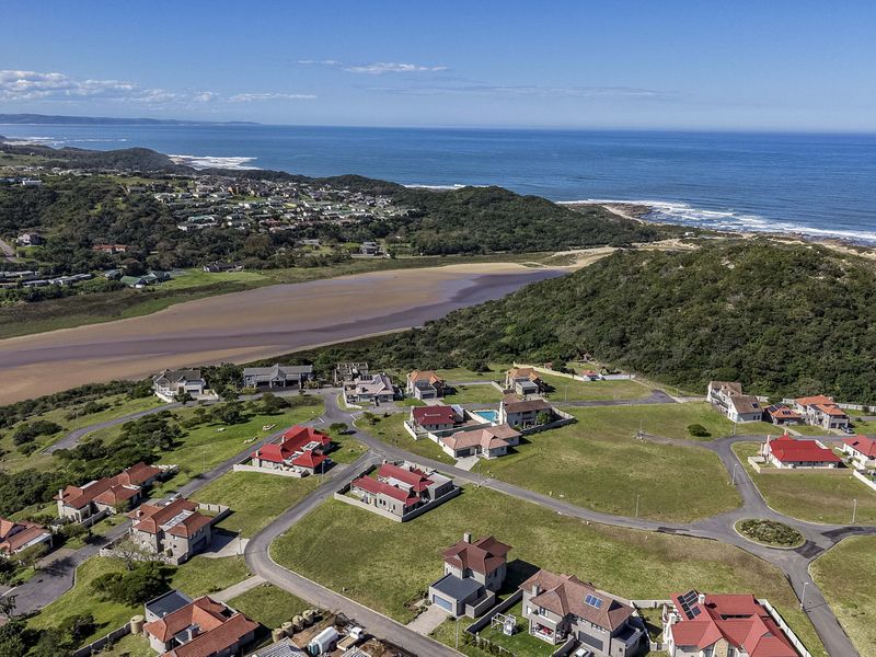Aerial view of a residential estate featuring vacant plots and established homes, situated near the coastline and natural landscape.