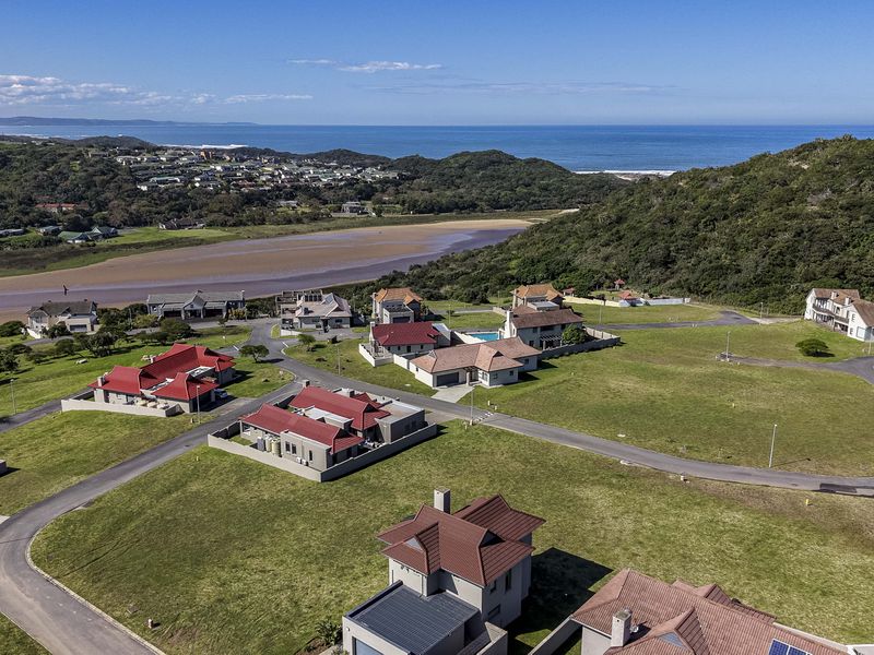 An aerial view of a residential estate featuring vacant plots, paved roads, and scenic coastal views.