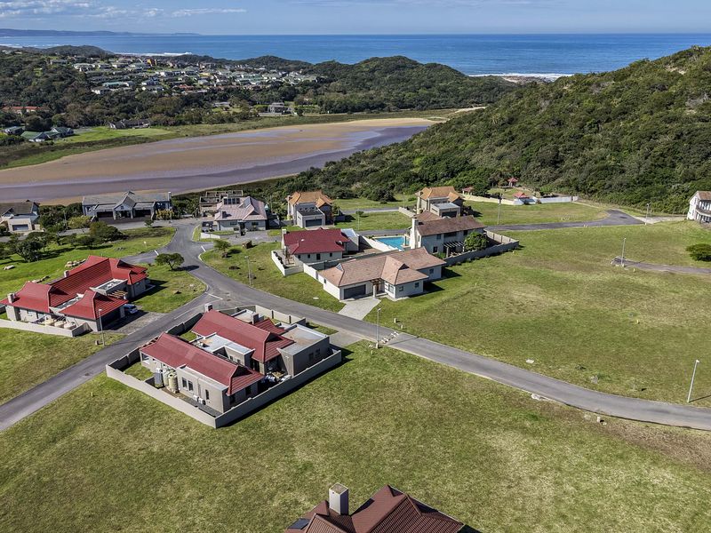 An aerial view of a residential estate featuring paved roads, established homes, and scenic views of the nearby estuary and coastline.
