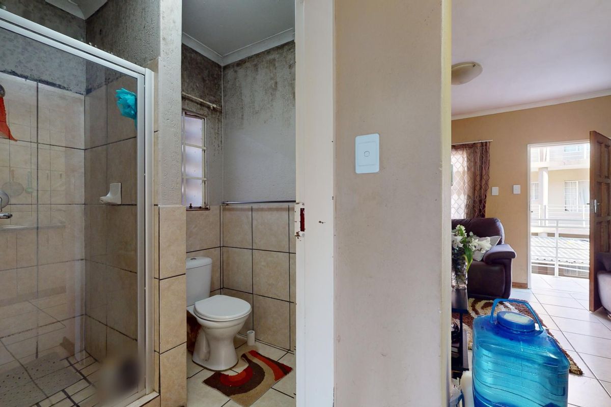 A compact bathroom featuring a shower enclosure and toilet, currently showing significant wall surface deterioration requiring maintenance and cosmetic repair.