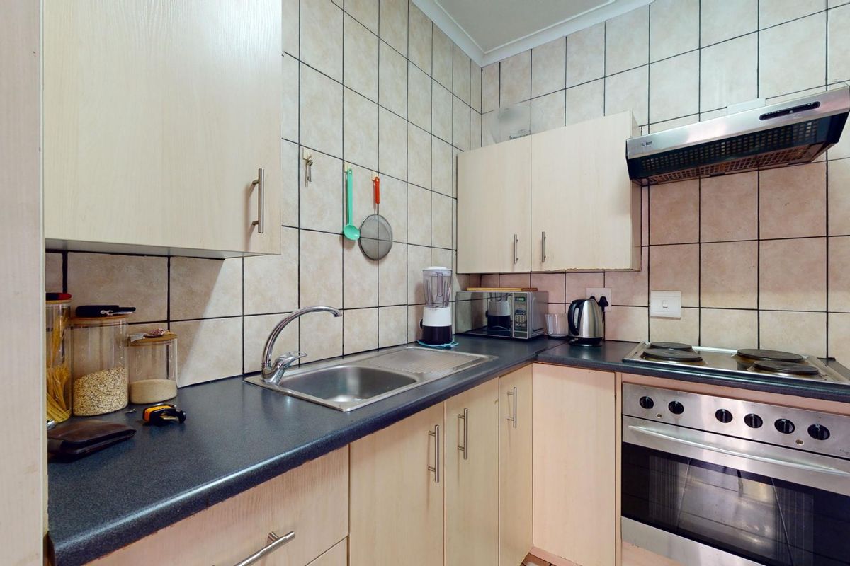 A functional kitchen featuring light wood-finish cabinetry, dark laminate countertops, a built-in oven with hob, and full-height ceramic wall tiling.