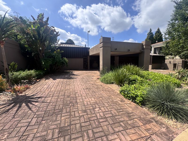 Front exterior view featuring a paved driveway, covered carport, and established landscaped garden with boundary walls.