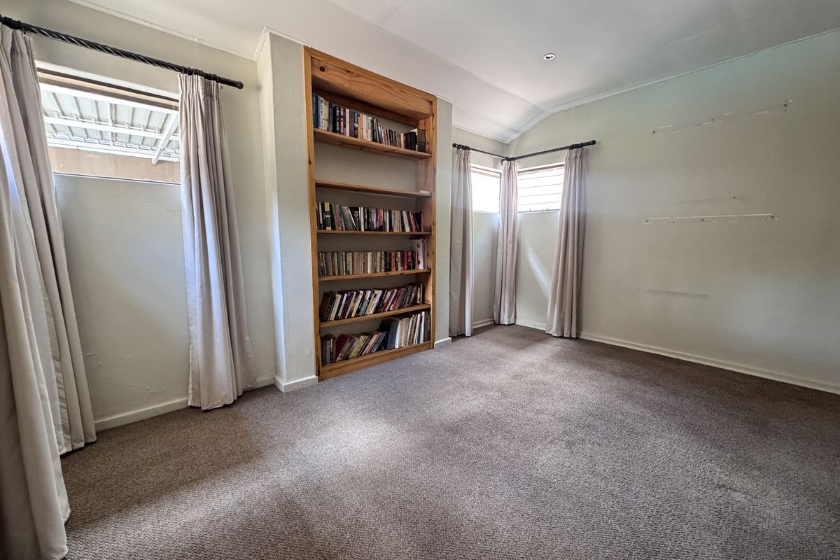 A spacious bedroom featuring neutral carpeting, built-in wooden shelving, and multiple windows providing natural light.