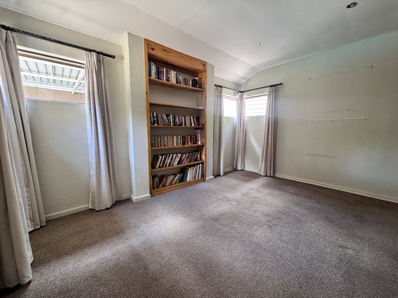 A spacious bedroom featuring neutral carpeting, built-in wooden shelving, and multiple windows providing natural light.