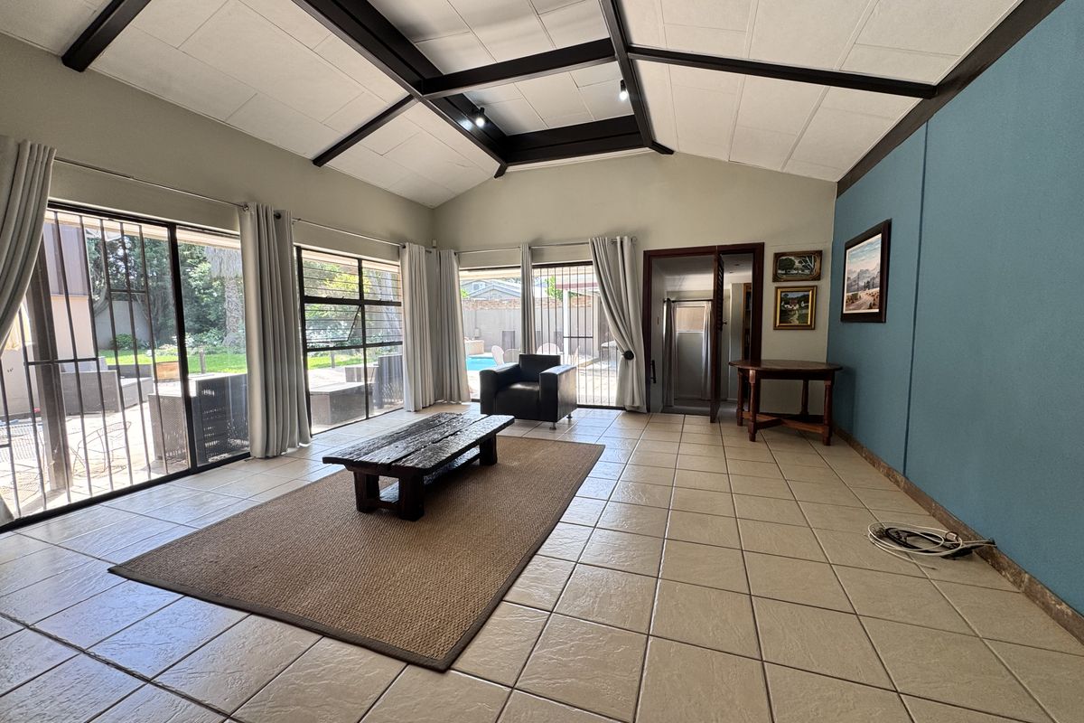 Spacious living room featuring a vaulted ceiling with exposed beams, large sliding glass doors with security gates, and neutral tiled flooring.