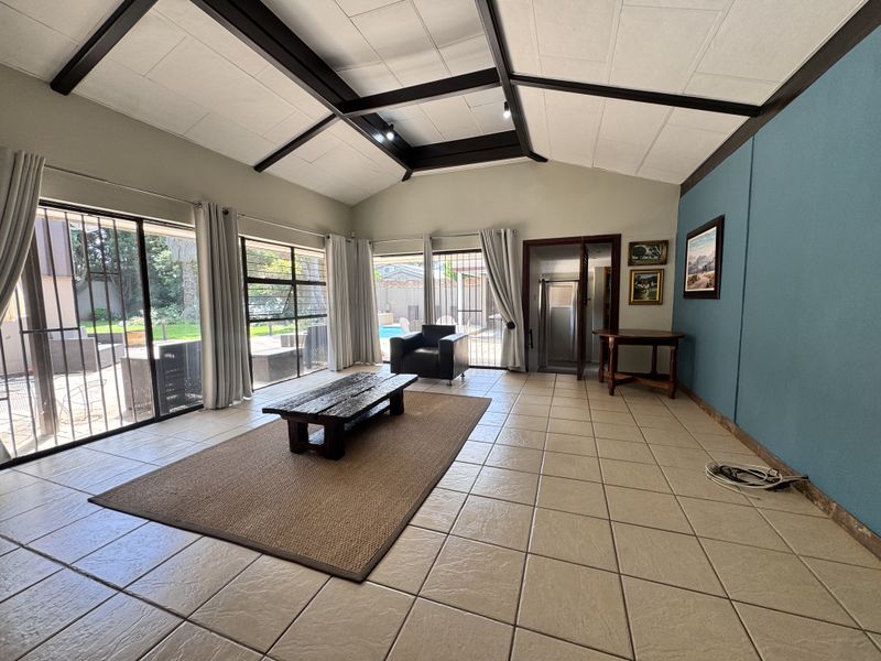 Spacious living room featuring a vaulted ceiling with exposed beams, large sliding glass doors with security gates, and neutral tiled flooring.
