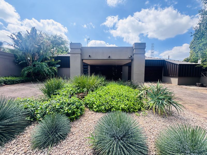 A modern front facade featuring a paved driveway, covered entrance, and well-maintained landscaped garden with mature shrubs and succulents.