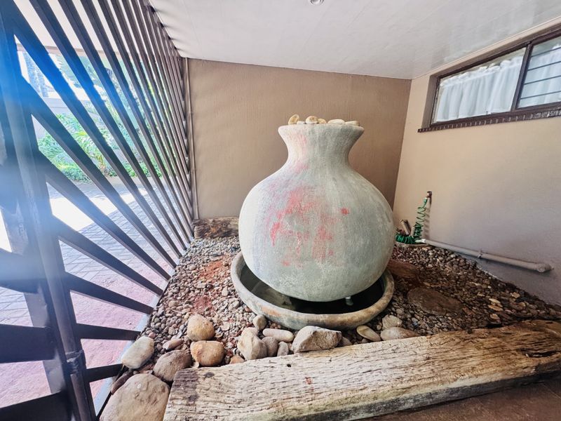 A covered patio area featuring a decorative stone water feature, pebble landscaping, and a timber privacy screen.