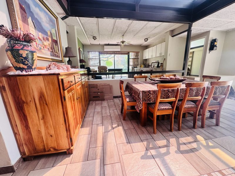 Spacious open-plan dining and living area featuring tiled floors, exposed ceiling beams, and direct access to the outdoor space through sliding glass doors.