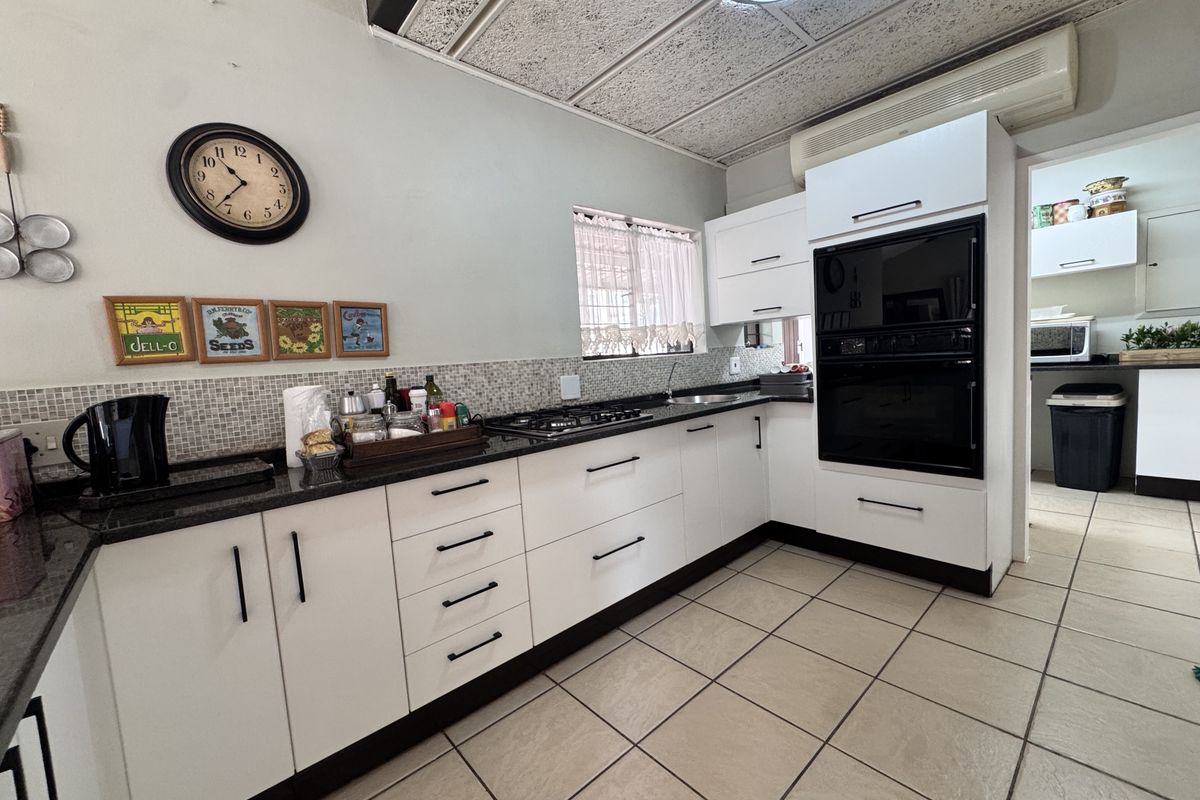 A well-maintained kitchen featuring modern white cabinetry, granite countertops, a built-in oven, gas hob, and tiled flooring with a mosaic backsplash.