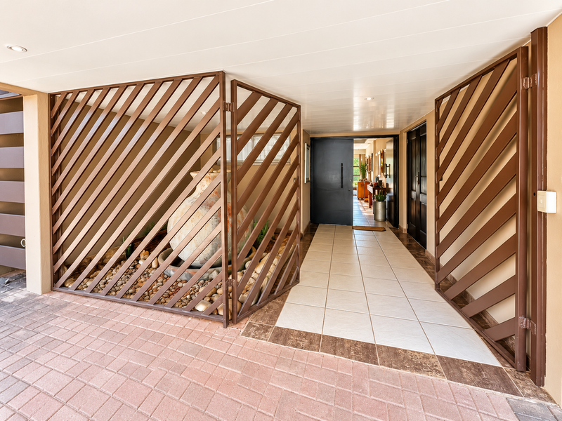 A welcoming entrance area featuring a modern pivot front door, decorative metal security screening, and clean tiled flooring leading into the home.