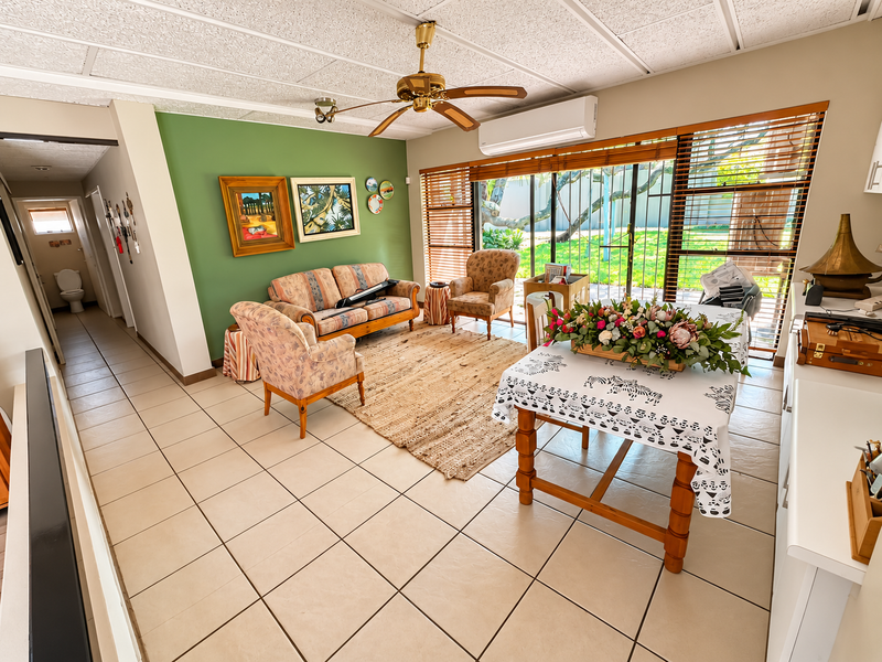 Open plan living and dining area featuring tiled floors, a ceiling fan, split system air conditioning, and large sliding doors leading to the garden.