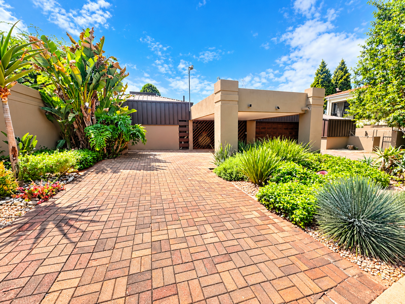 A well-maintained front exterior featuring a paved driveway, covered carport, and established landscaped garden with mature plantings.