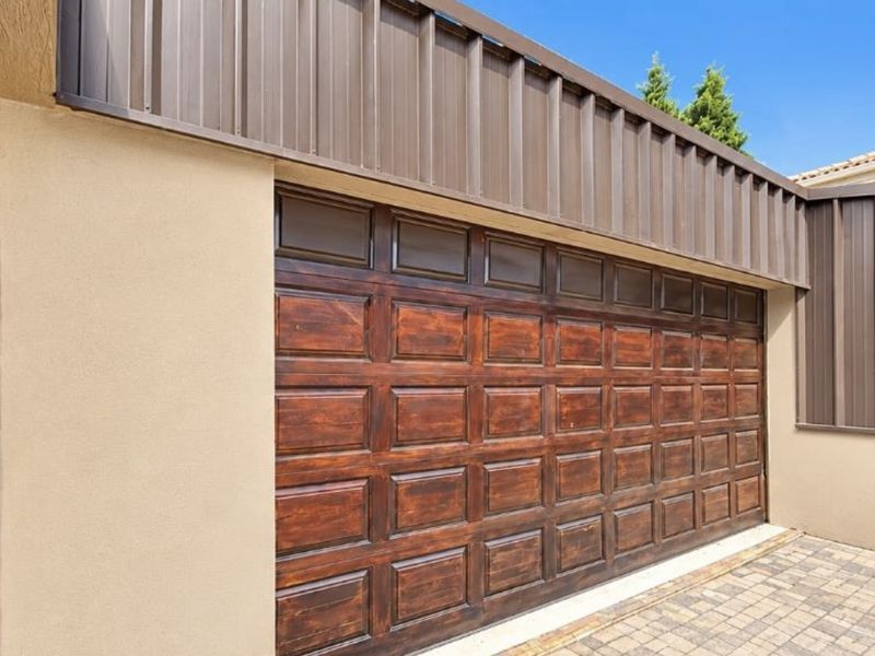 A well-maintained garage exterior featuring a dark wood-finish sectional door, modern metal cladding, and neat paved driveway.