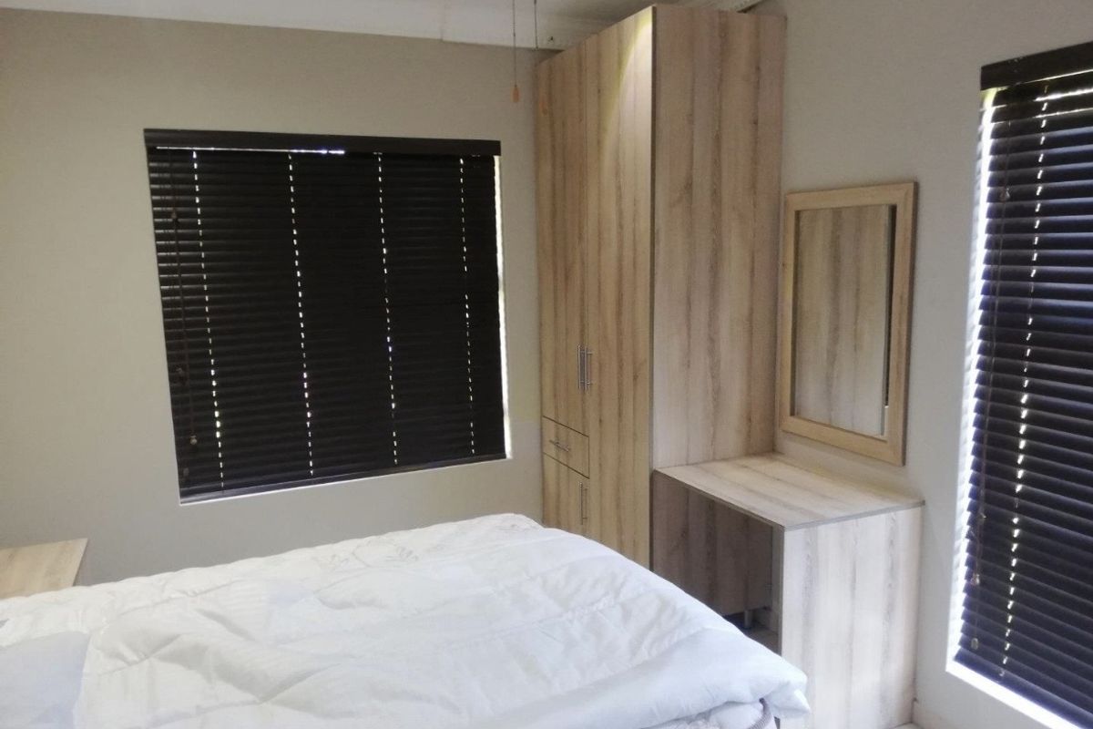 A well-maintained bedroom featuring built-in light wood cabinetry, a matching vanity unit, and dark venetian blinds.