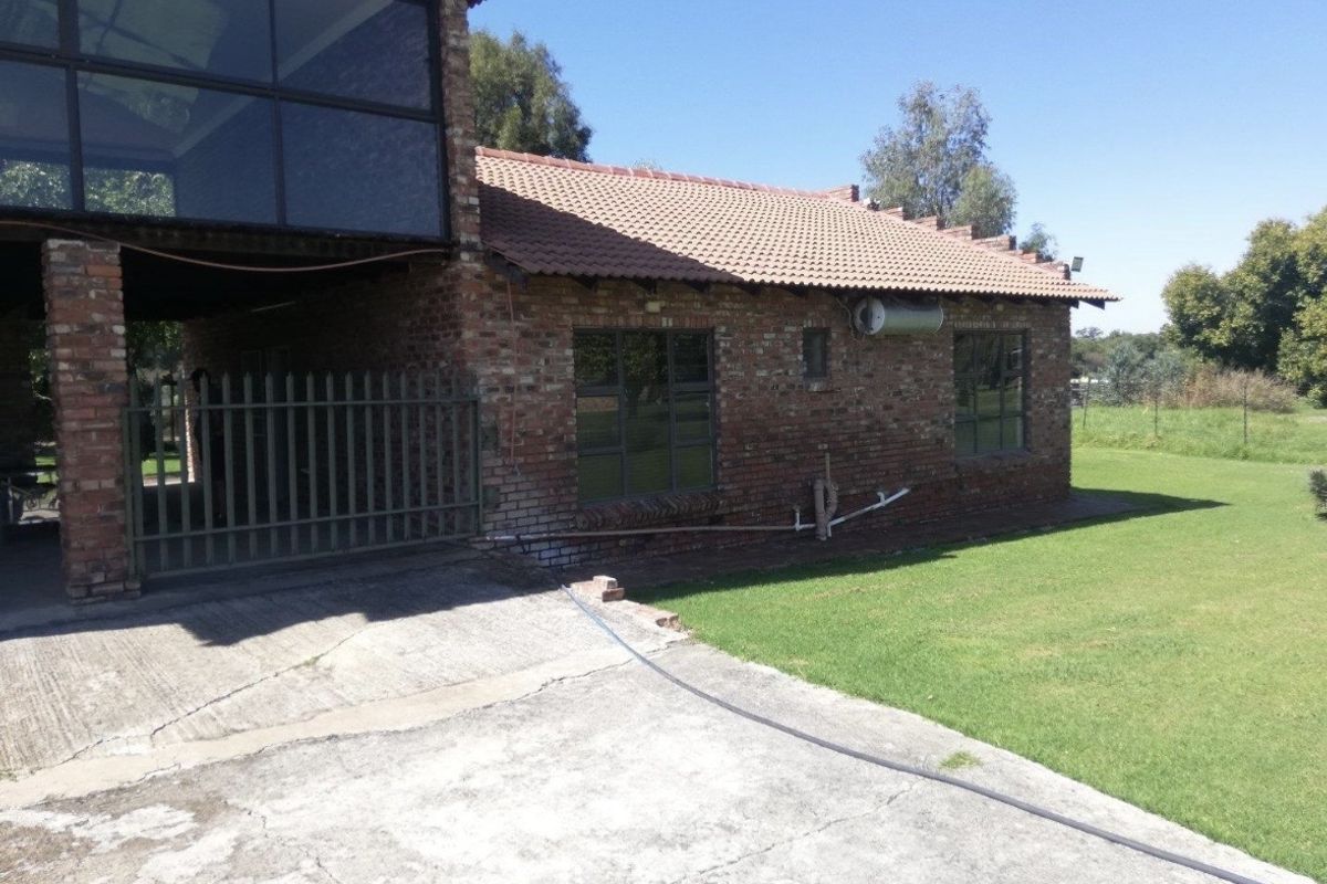 Rear view of a rustic brick farmhouse featuring a tiled roof, concrete driveway, and established garden surroundings.