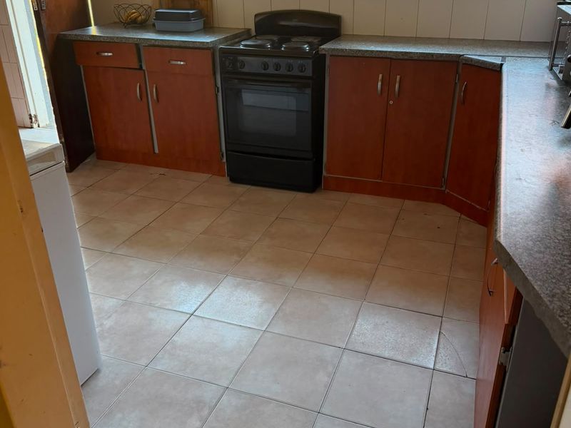 A functional kitchen featuring wooden cabinetry, laminate countertops, a freestanding stove, and tiled flooring with security bars on the windows.
