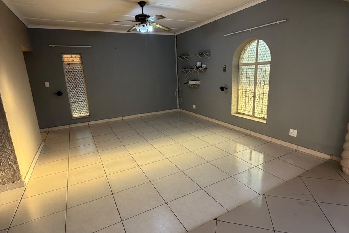 An empty living room featuring tiled flooring, a ceiling fan, and an arched window with security grilles.