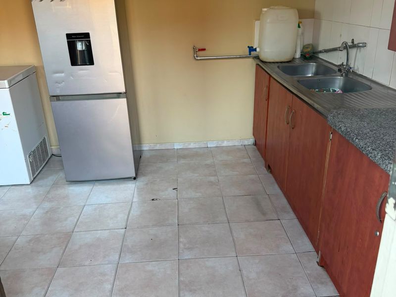 A functional kitchen area featuring base cabinetry, a double sink, tiled backsplash, and tiled flooring, requiring cosmetic updates to improve its overall aesthetic.