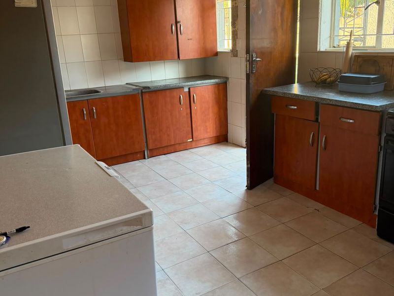 A functional kitchen featuring wood-look cabinetry, laminate countertops, tiled flooring, and a window with security bars, offering potential for a modern update.