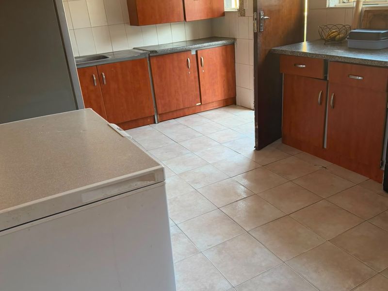 A functional kitchen featuring wood-look laminate cabinetry, tiled flooring, and tiled splashbacks, offering a practical layout with ample storage space.