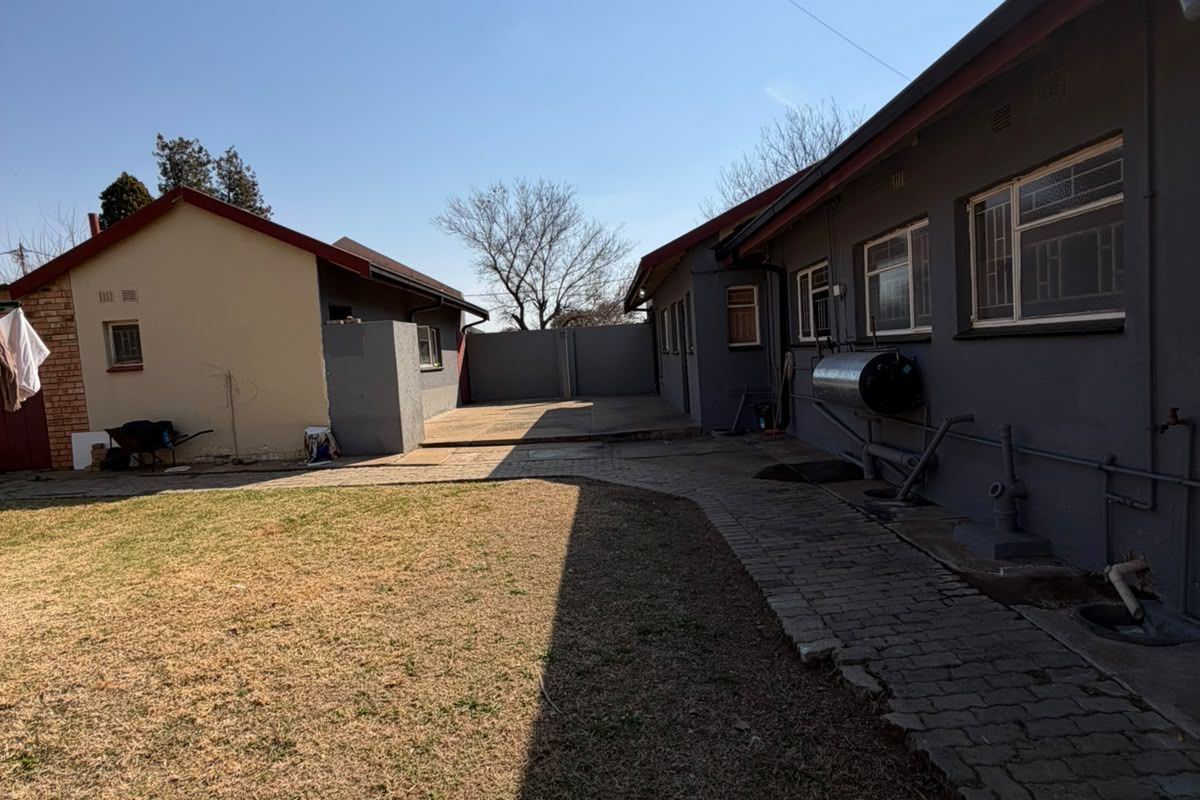 Rear exterior view of the property featuring a paved walkway, lawn area, and external geyser installation.