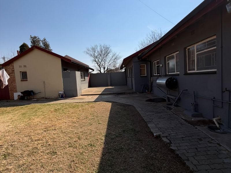 Rear exterior view of the property featuring a paved walkway, lawn area, and external geyser installation.