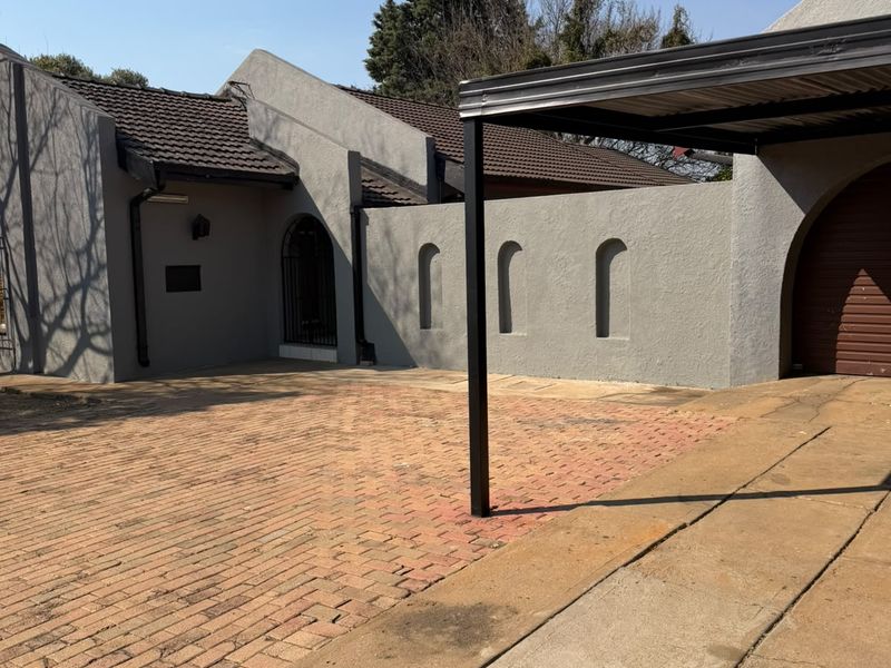 Front exterior view featuring a brick paved driveway, a carport, and a grey rendered facade with distinctive arched architectural details.