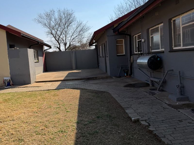 Rear exterior view of the property featuring a paved walkway, concrete patio area, and external geyser unit against the main building structure.