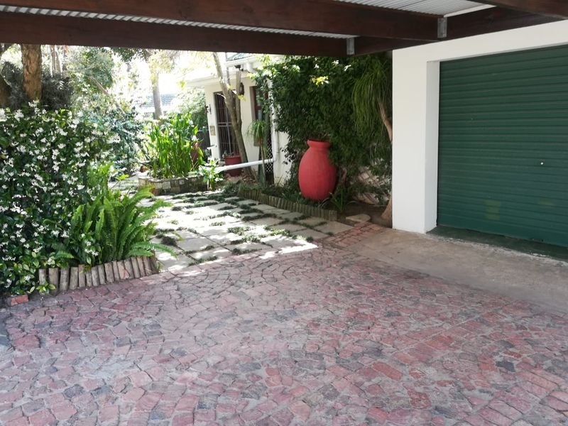 A covered carport area featuring a green garage door and a charming cobblestone driveway leading to a landscaped garden path.
