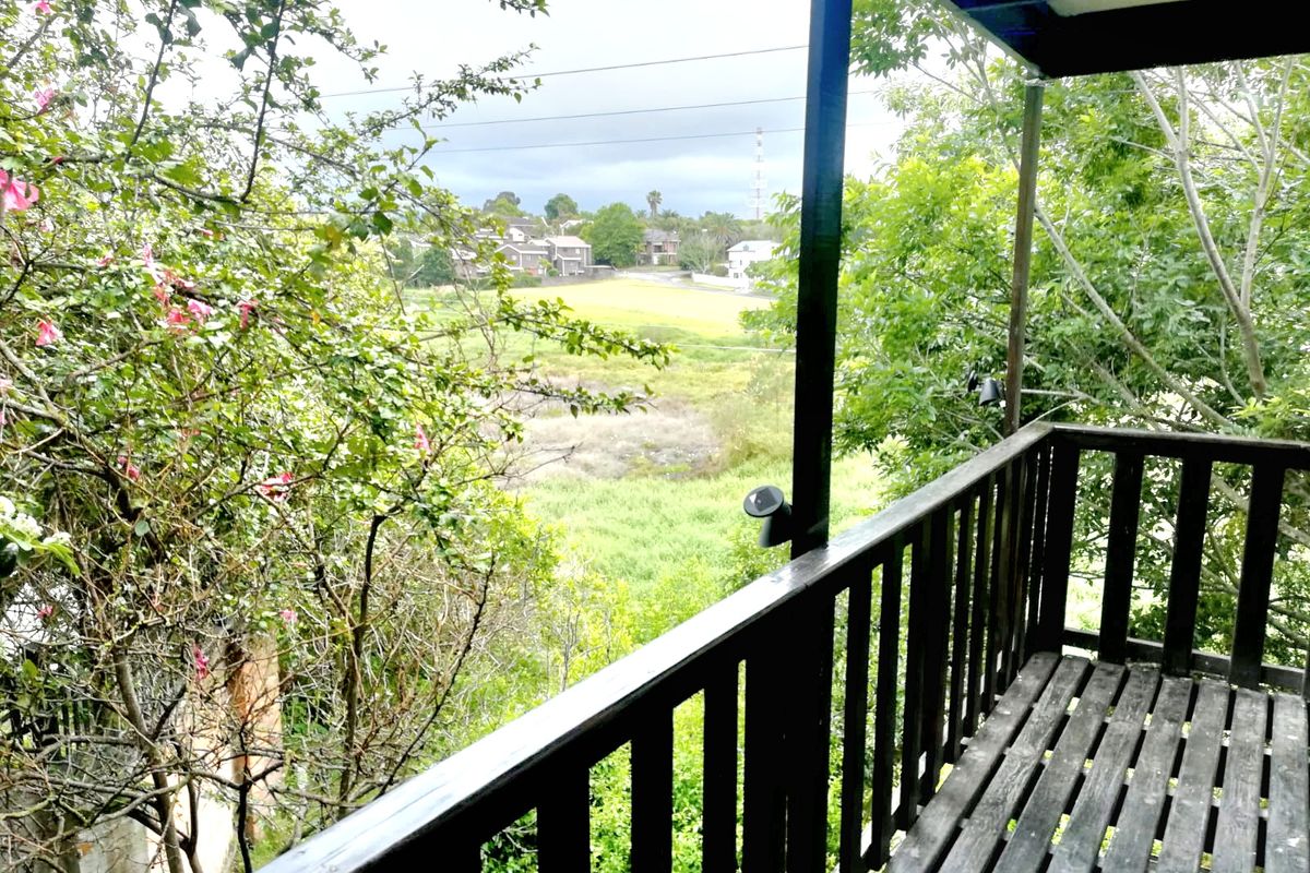 An elevated timber balcony featuring a wooden balustrade and decking, offering an open view of the surrounding greenery and neighborhood.